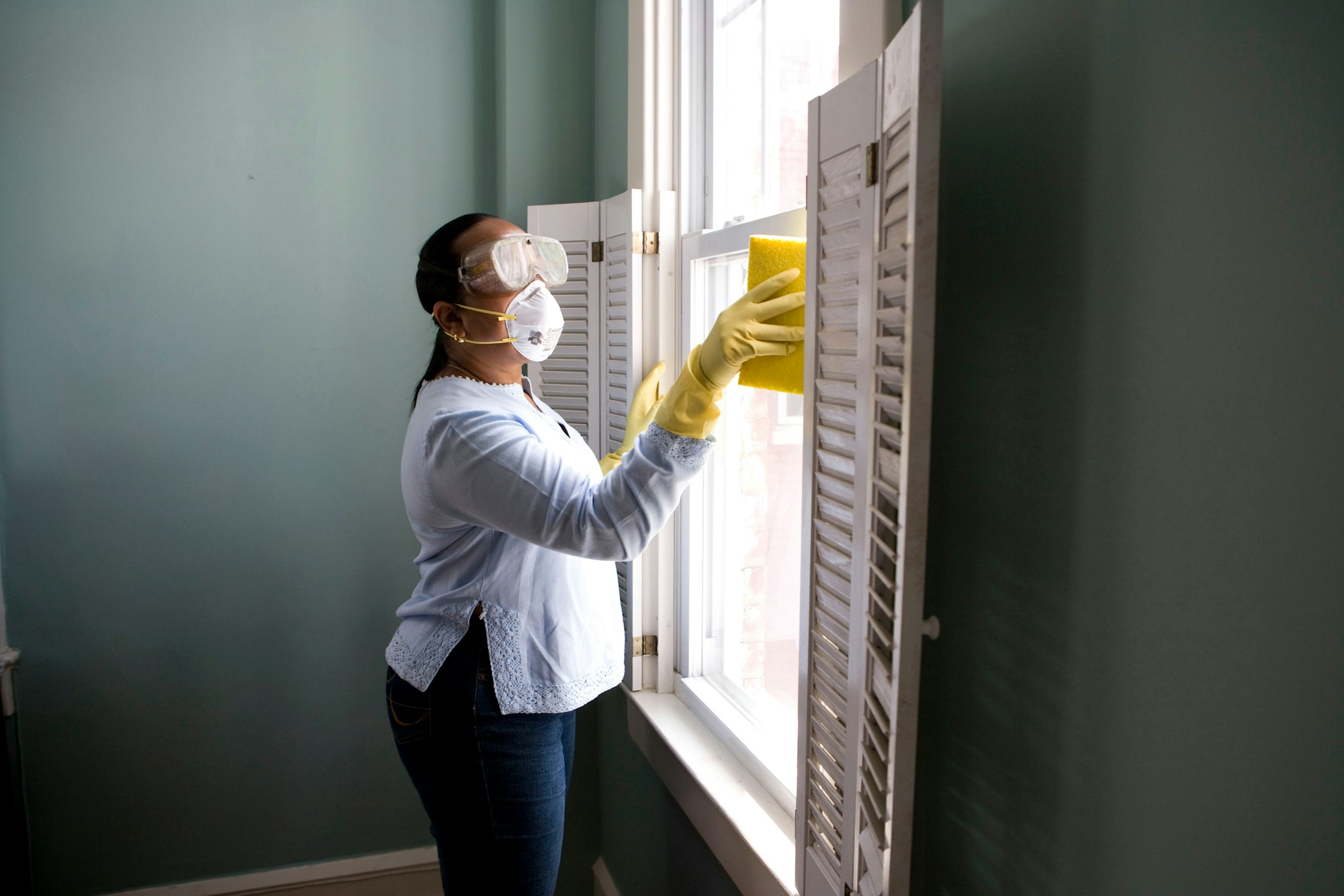 Professional cleaner wiping window shutters with yellow sponge - Edislo Cleaning LLC providing quality cleaning services